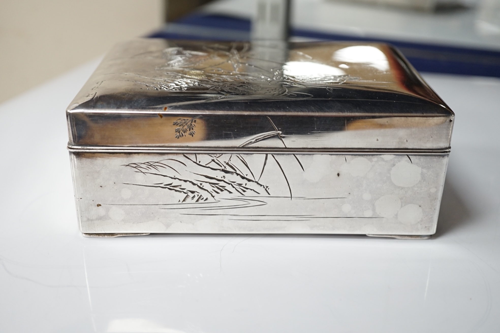 A Japanese white and yellow metal mounted rectangular cigarette box, engraved with birds and reeds, signed to the base, 14.2cm. Condition - fair